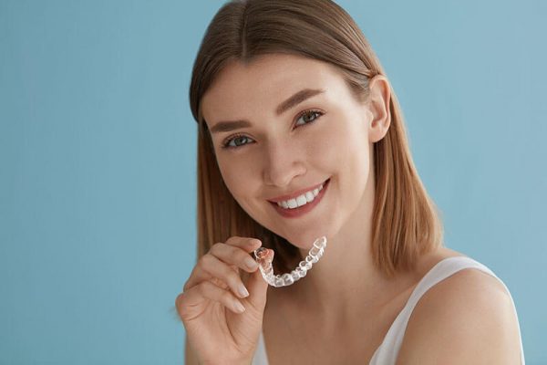 young woman smiling and holding Invisalign aligners