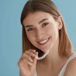 young woman smiling and holding Invisalign aligners